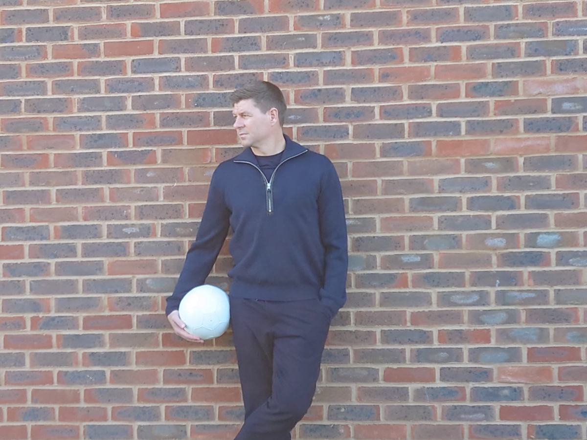 Steven Gerrard holding a football against a brick wall